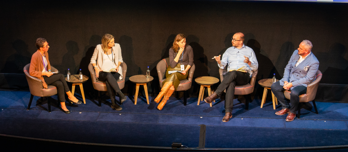 Panel discussion featuring five speakers seated on stage, sharing insights and engaging in conversation.
